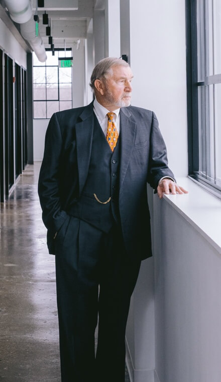 Robert Wagner stands near a window in an office building. He is wearing a suit and looking out the window confidently.
